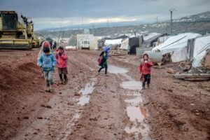Group of children walking through a muddy path in a refugee camp in Idlib, Syria.